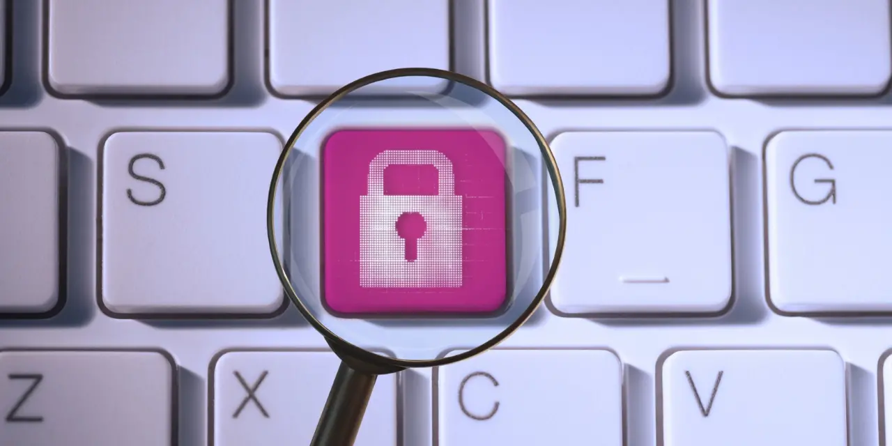 Keyboard with pink padlock key seen through magnifying glass.