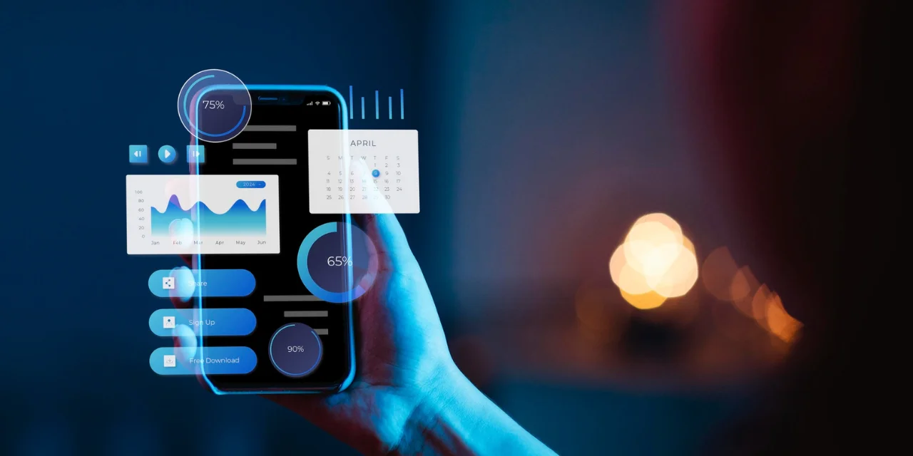 The image shows a hand holding a smartphone, with a futuristic digital interface projected onto the screen. Augmented reality graphic elements appear floating around the device, including line graphs, virtual buttons (“Share”, “Sign Up”, “Free Download”), circular progress indicators with percentages (65%, 75%, 90%), a calendar highlighting the month of April and data bars. The background is blurred, with dark tones and out-of-focus yellowish circular lights, creating a technological and modern environment. The image represents digital innovation, interactivity and the use of advanced technology.