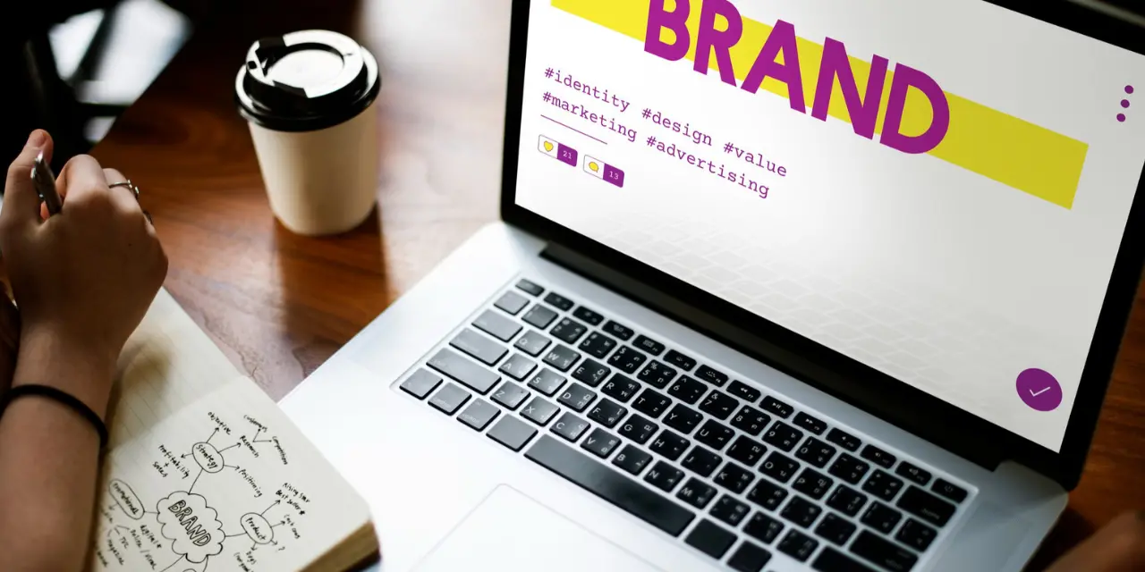 Tela de laptop exibindo a palavra "BRAND" e hashtags de marketing.