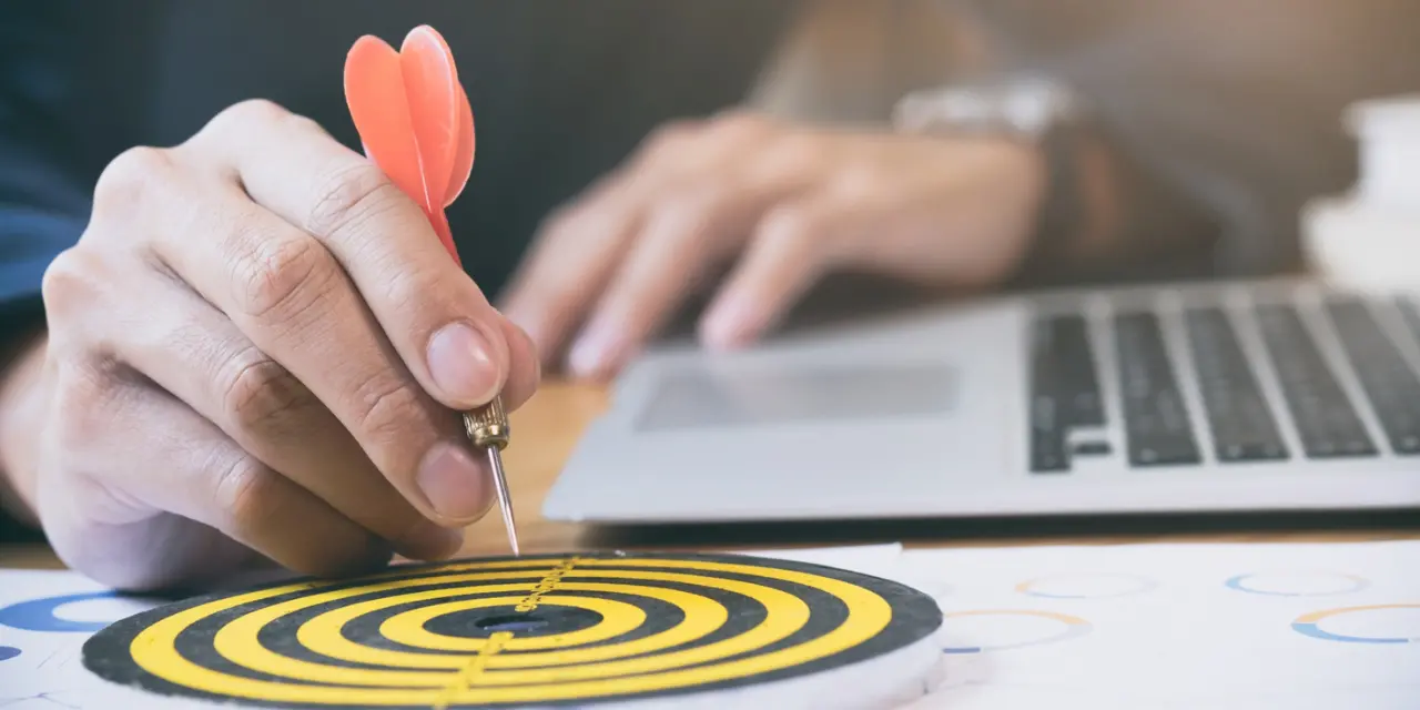 Hand holding a dart in the center of a target, symbolizing focus on goals.