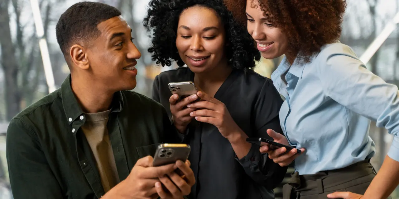 Three young professionals smiling and networking using their smartphones, sharing digital business cards in a modern office setting.