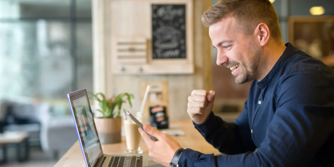 Empreendedor sorrindo ao compartilhar seu cartão de visita digital pelo smartphone enquanto trabalha no notebook.